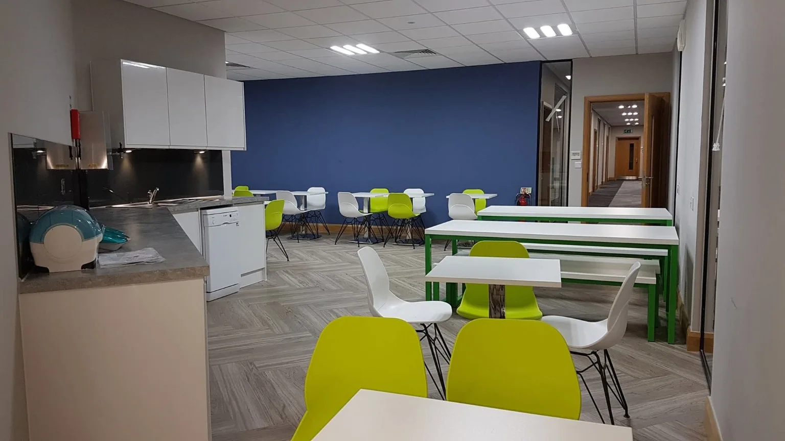 Clean staff kitchen and dining area with green and white chairs